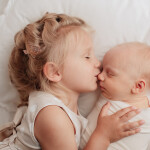 старшая сестра целует маленького брата в пеленке