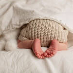 маленькие ножки новорожденного твыглядывают из одела лежит на животике
