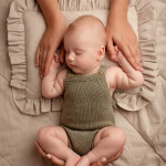 малыш спит в зеленом вязанном боди на ажурной подушке родительские руки держат ребенка