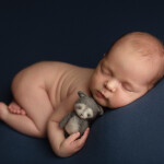 новорожденный лежит на синем пледе обнимает игрушку