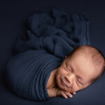 новорожденный малыш укутан в синюю обмотку марлю лежит на синей ткани