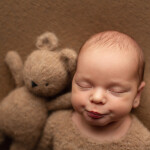 портрет новорожденного ребенка на коричневом фоне с вязаным мишкой