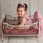ребенок смеется в металлической кроватке в розовой кофточке на белых деревянных досках